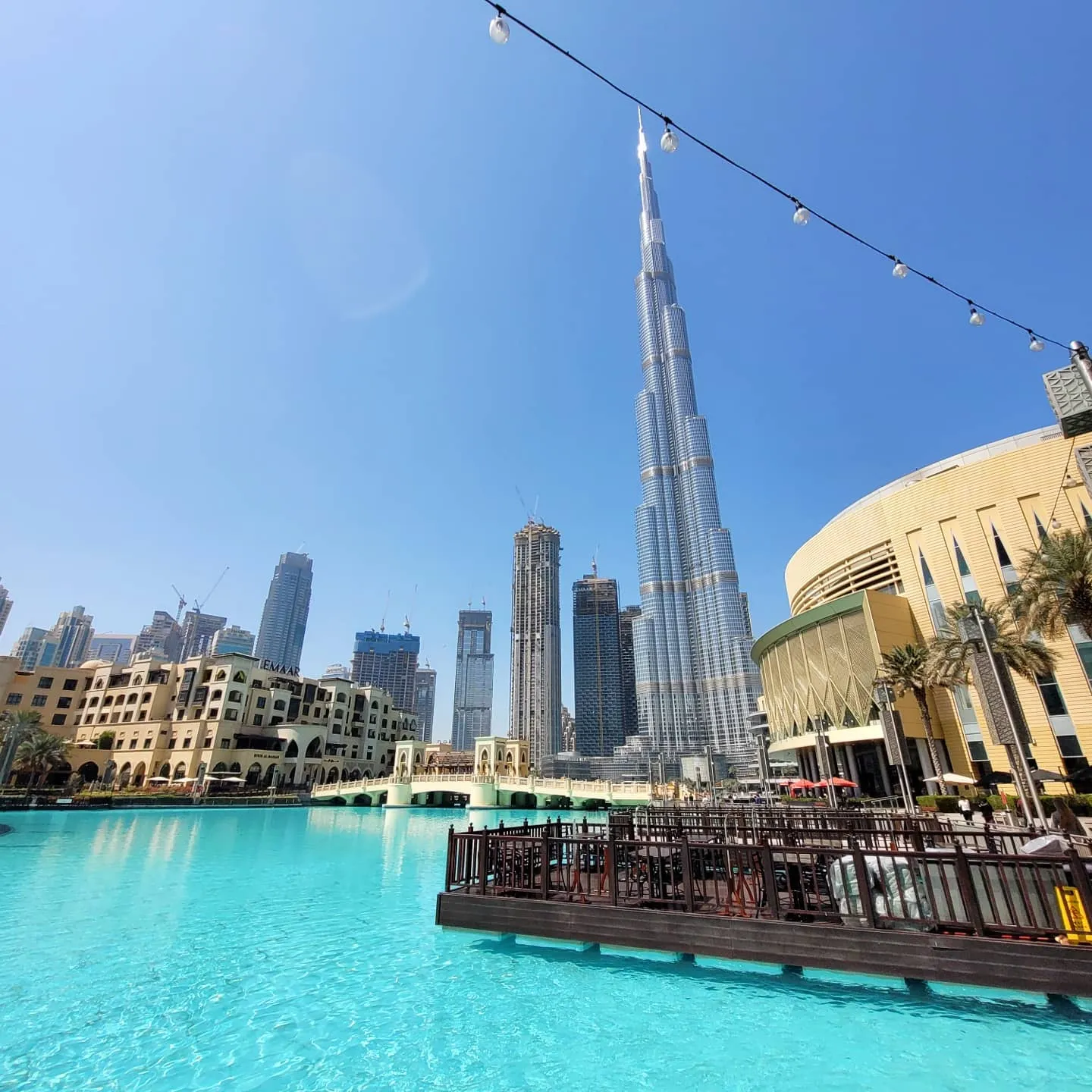 Burj Khalifa rising above the turquoise fountain lake by Dubai Mall on a clear day