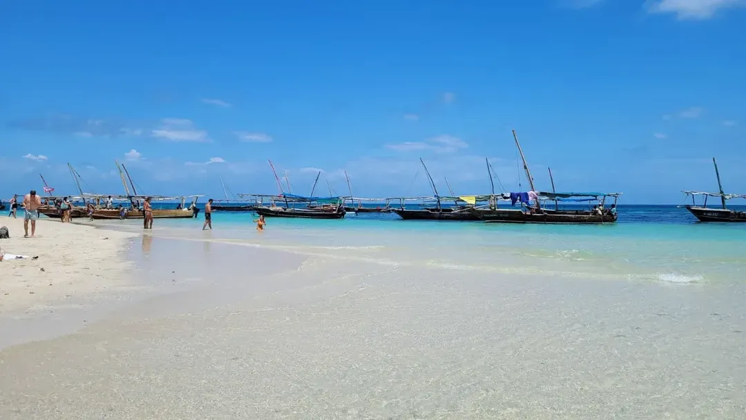 Traditional wooden dhow boats anchored in a line off a white sandbank under a deep blue sky