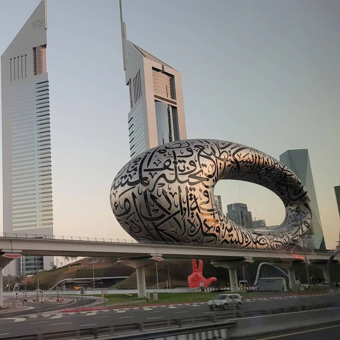 The torus-shaped Museum of the Future covered in Arabic calligraphy, with Emirates Towers behind it at dusk