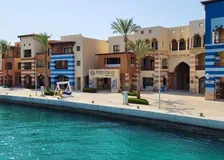 Waterfront promenade at Port Ghalib marina with striped orange-and-blue buildings and palm trees over turquoise water