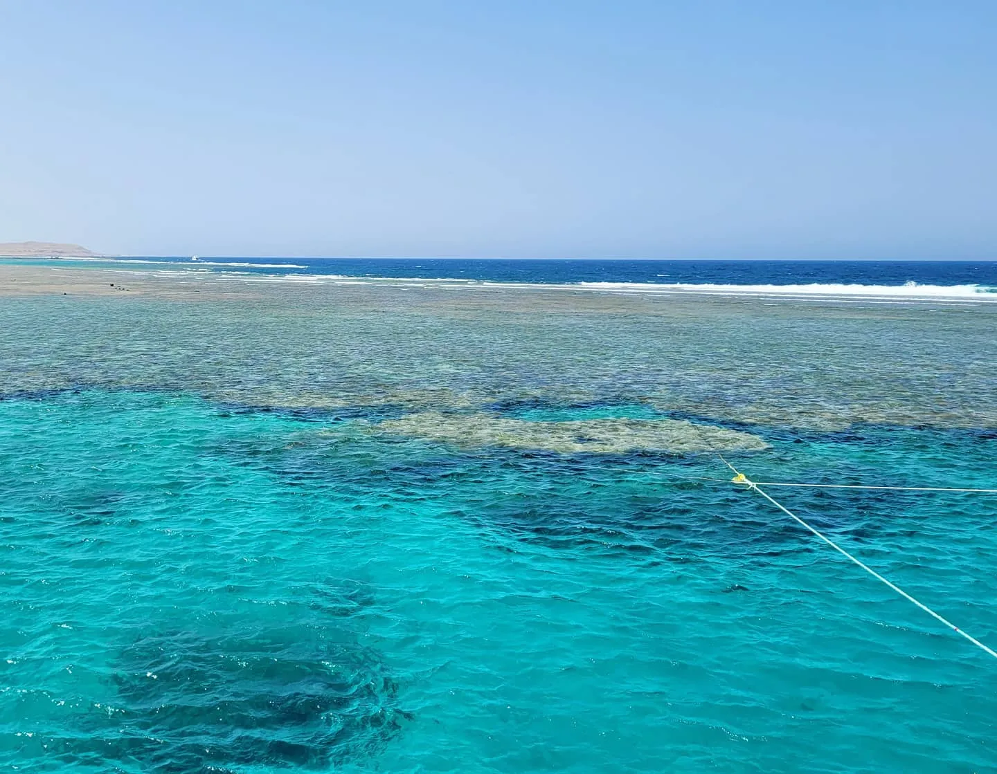 Coral reef under shallow turquoise water with dark blue open sea and breaking waves behind it