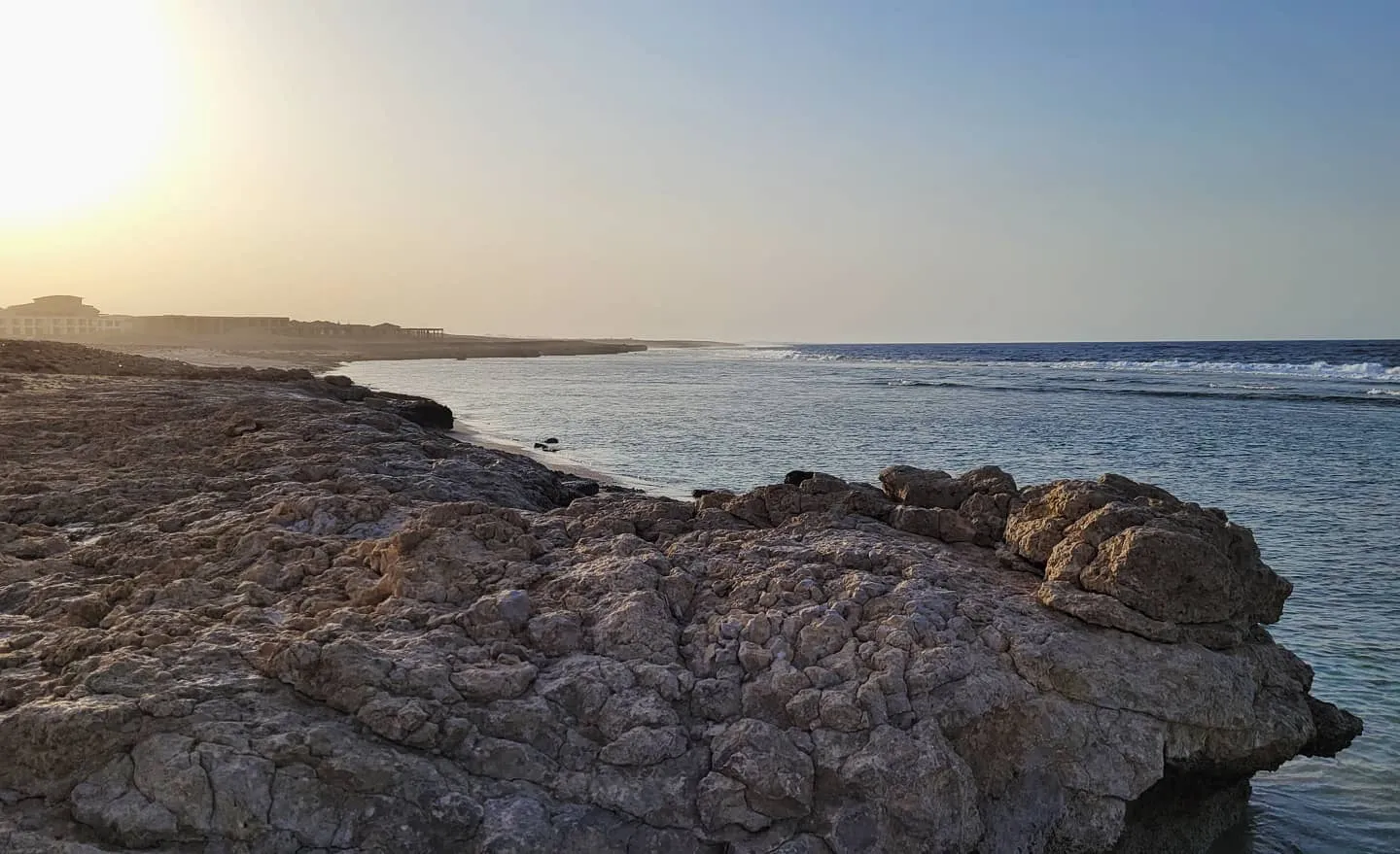 Fossil coral rock shoreline at golden hour with a calm bay and resort buildings in the haze