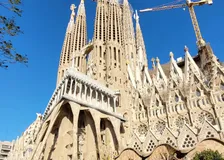 Passion façade of the Sagrada Família with its towers and construction cranes against a deep blue sky