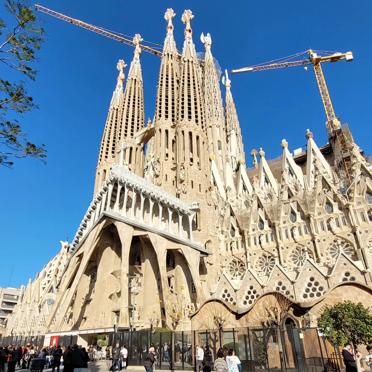 Passion façade of the Sagrada Família with its towers and construction cranes against a deep blue sky