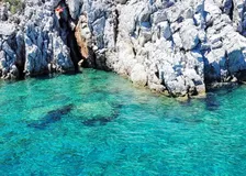Small cove of glassy turquoise water below jagged white limestone rocks with a Turkish flag planted on top
