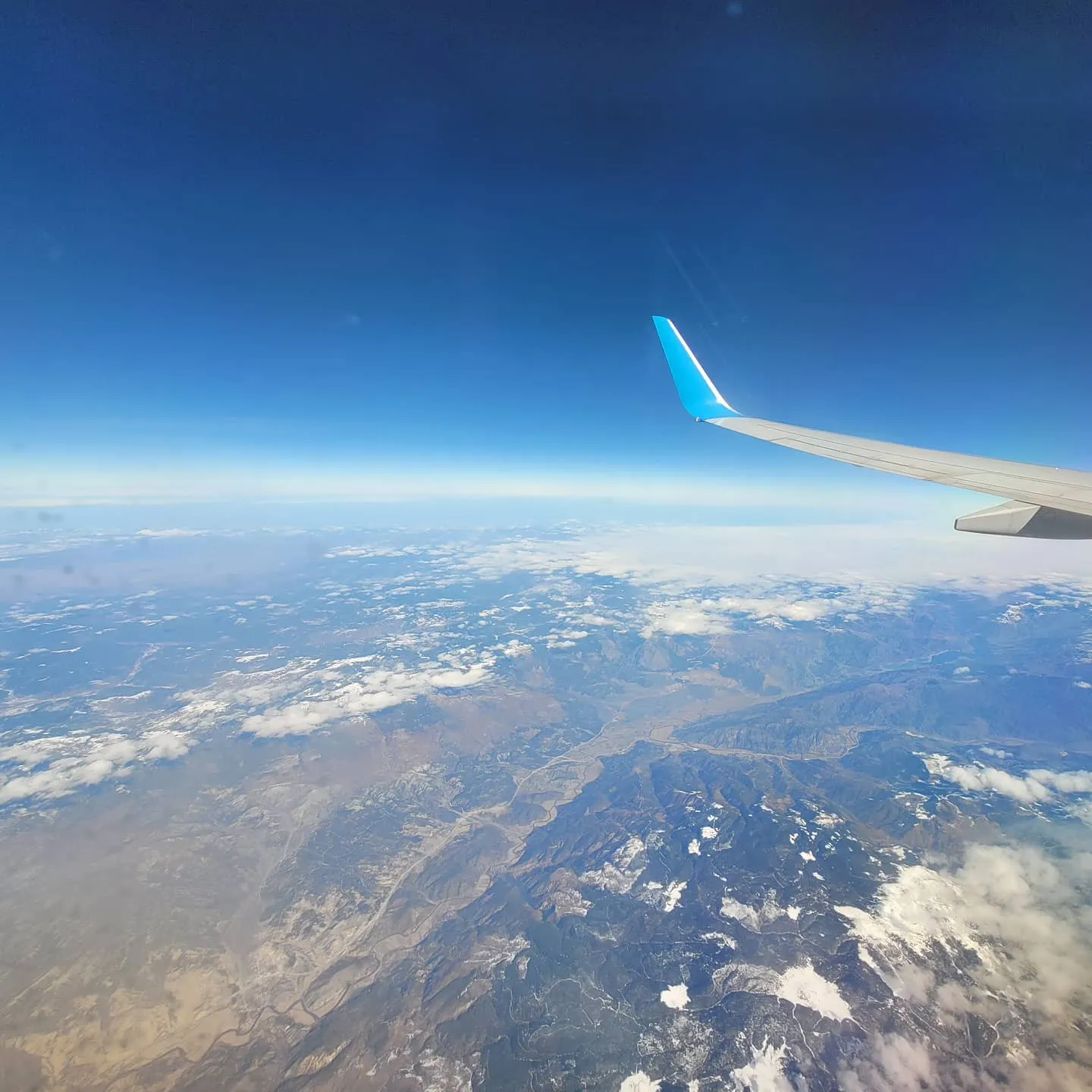 Winglet over snow-dusted mountain ridges and river valleys under a deep blue gradient sky